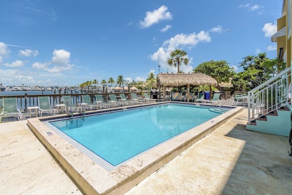 A rectangular swimming pool with a clear blue water, surrounded by lounge chairs and a thatched-roof structure.