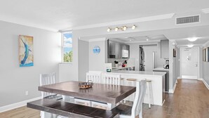 A modern kitchen with white cabinets, a central island, and a dining area with a wooden table and white chairs. - Waterfront Dock Pool Key West Near Duval (Key West)
