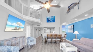 A spacious living area with a dining table, a ceiling fan, and a large painting of a sailboat on the wall.