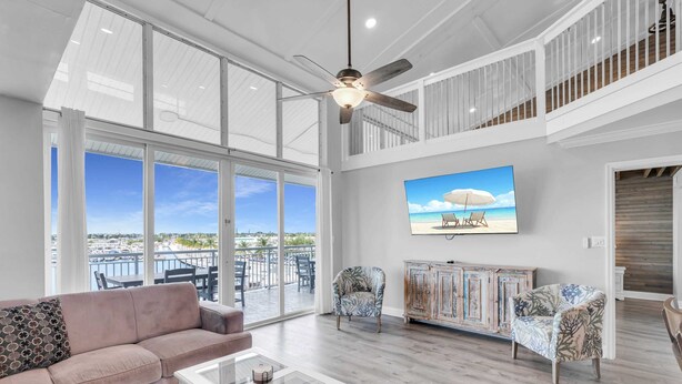 A spacious living room with a large window, a ceiling fan, and a view of the ocean.