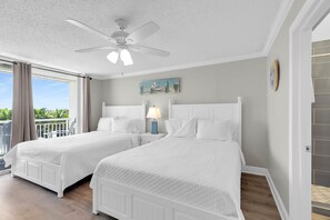 Quarto de hotel com duas camas, um ventilador de teto, uma varanda com cortinas e um quadro na parede.