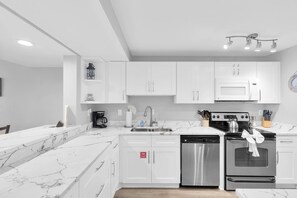 A modern kitchen with white cabinetry, a marble countertop, stainless steel appliances, and a 'FIRE ALARM' sign on the door. - Penthouse Waterfront Dock Pool Condo Near Duval St (Key West)