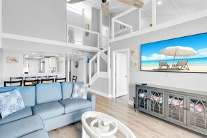 A spacious living area with a high ceiling, a dining area, and a staircase leading to an upper level.