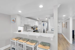 A modern kitchen with white cabinets, a marble countertop, and a built-in washing machine.