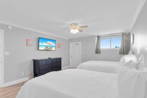 Quarto com duas camas, ventilador de teto, televisão e janela com cortinas.