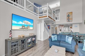 Un salon spacieux avec une grande télévision, un canapé bleu et un escalier menant à un niveau supérieur.