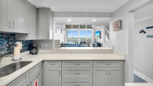 A modern kitchen with grey cabinets, a stainless steel sink, and a view to the dining area.
