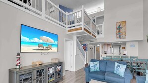 A spacious living room with a large TV, a blue sofa, and a staircase leading to an upper level.