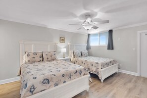 A bedroom with two beds, a ceiling fan, a window with curtains, and a nightstand with a lamp.
