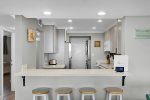 A modern kitchen with a central island, bar stools, and a welcome sign. - Waterfront Dock Pool Penthouse Near Duval St (Key West)