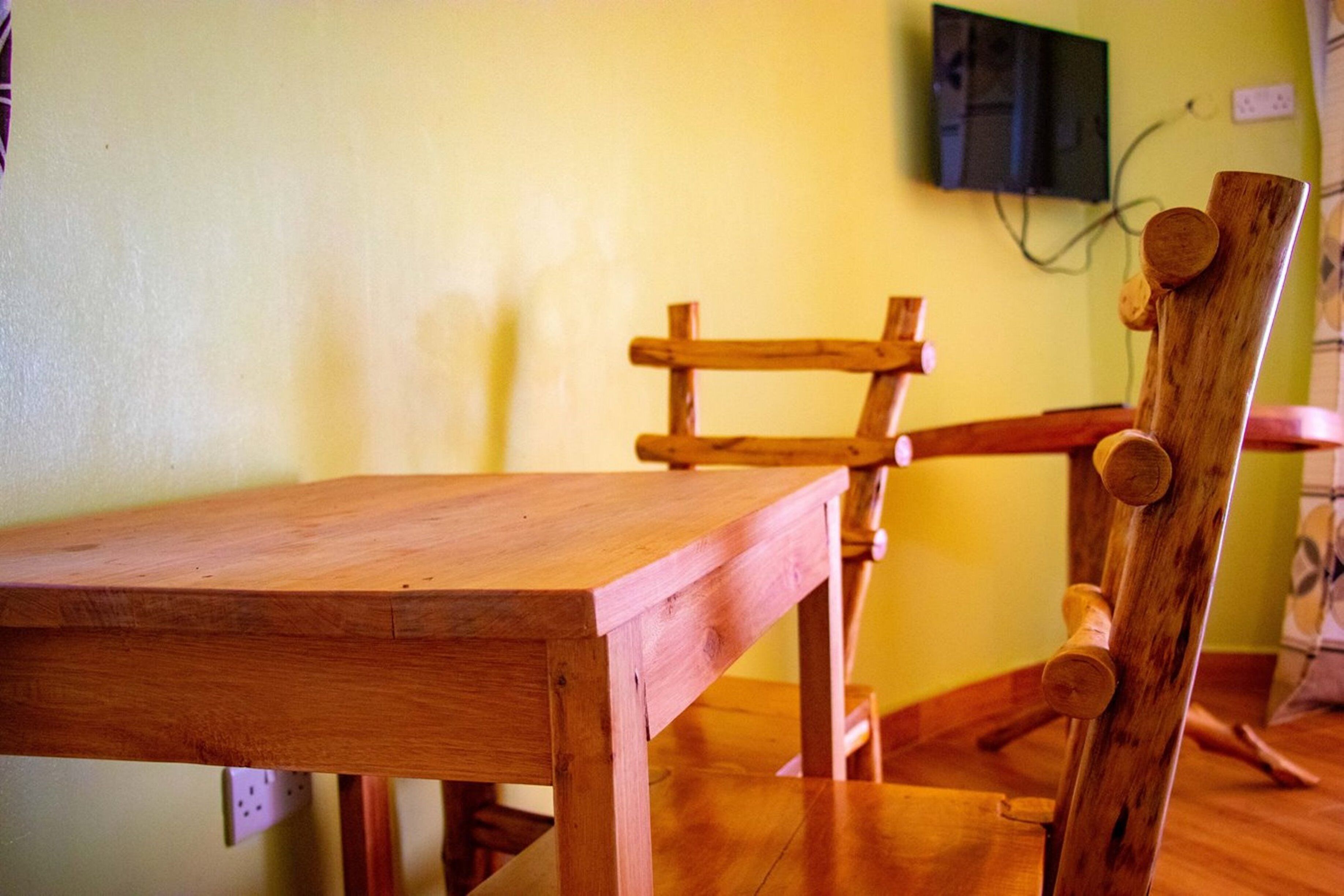 Una mesa de comedor de madera con sillas, un televisor montado en la pared y un enchufe.