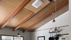 A kitchen with a wooden countertop, bar stools, a hanging pot rack, and a window with a view of greenery. - Charming Geneva Bungalow (Bellingham)