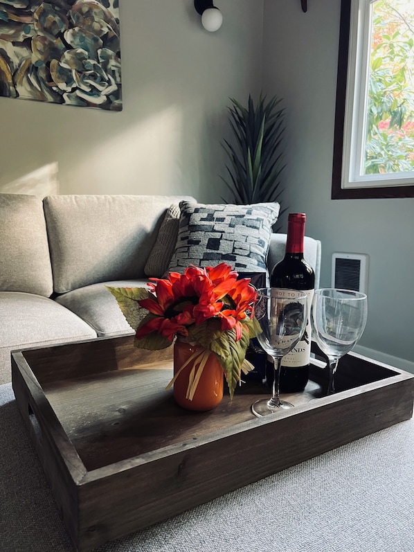 A wooden tray with a wine bottle and glasses on a sofa, a vase with red flowers, and a plant in the background. - Charming Geneva Bungalow (Bellingham)