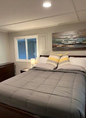Un dormitorio con una cama grande, una mesita de noche, una ventana y un cuadro en la pared.