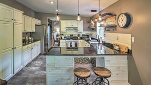 Une cuisine moderne avec des meubles blancs, un grand îlot central doté de tabourets, un éclairage suspendu et une horloge au mur.