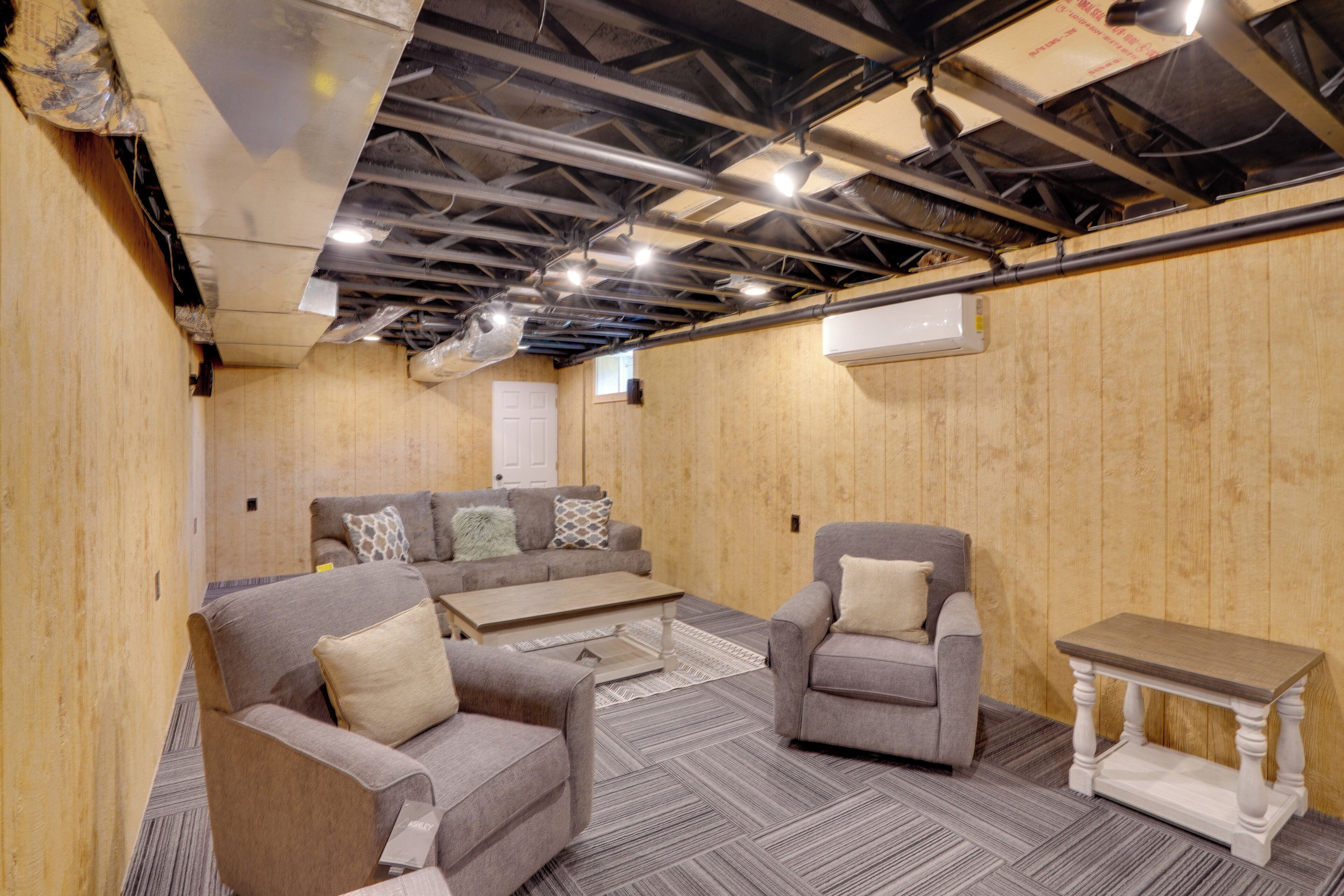 Ein Zimmer mit zwei Sofas, einem Couchtisch und einem kleinen Tisch. Die Wände sind aus Holz und die hohe Decke hat freiliegende Balken und Lüftungsrohre.