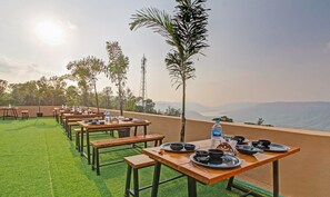 A rooftop dining area with tables set for meals, overlooking a scenic landscape. - Treebo Dreamworld (Mahabaleshwar)