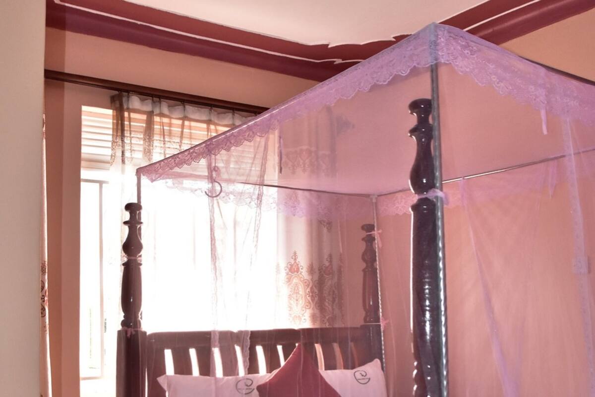 A four-poster canopy bed with a white bedspread and pillows, a wooden headboard, and a pink furry rug on the floor.