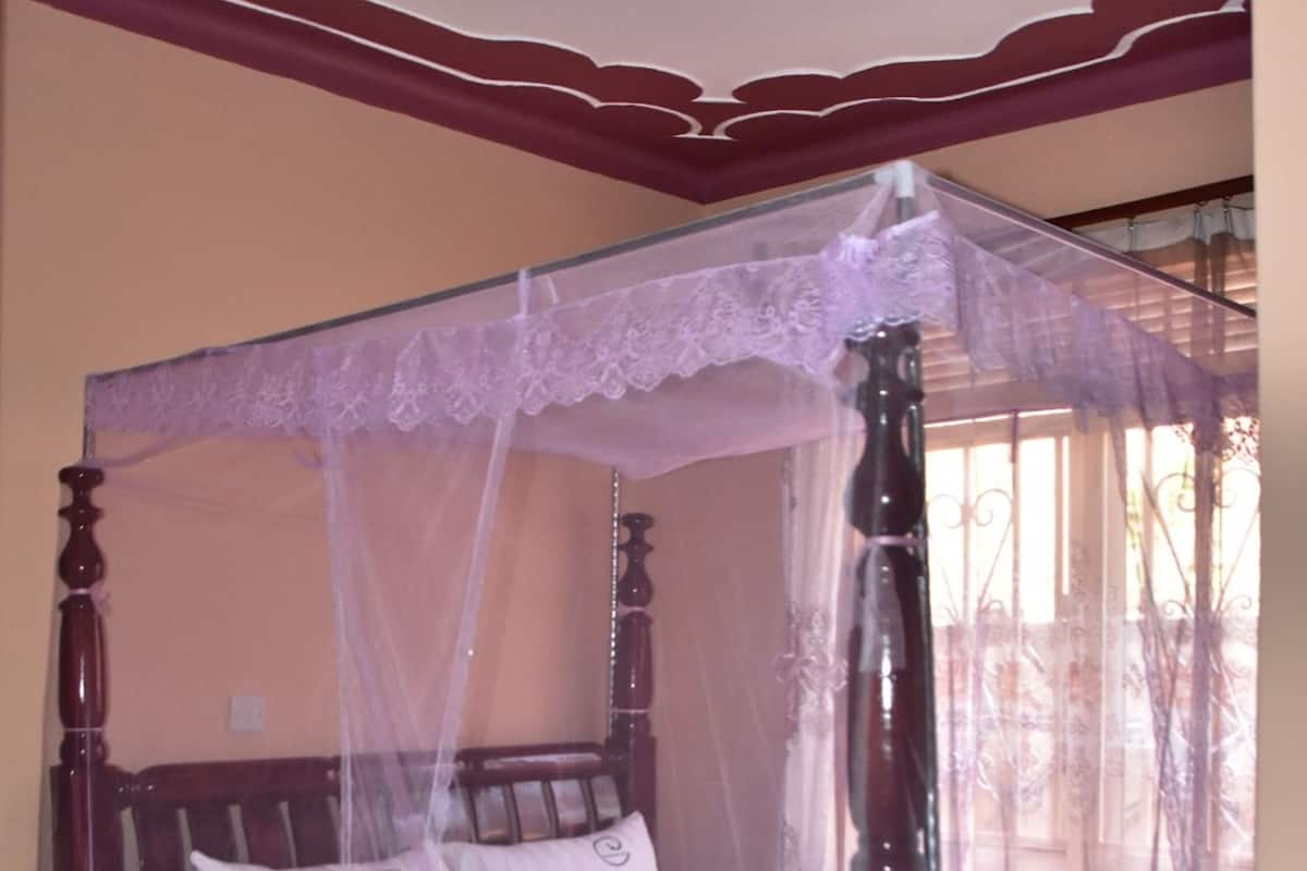 A four-poster canopy bed with a lace canopy, wooden headboard, and a floral bedspread.