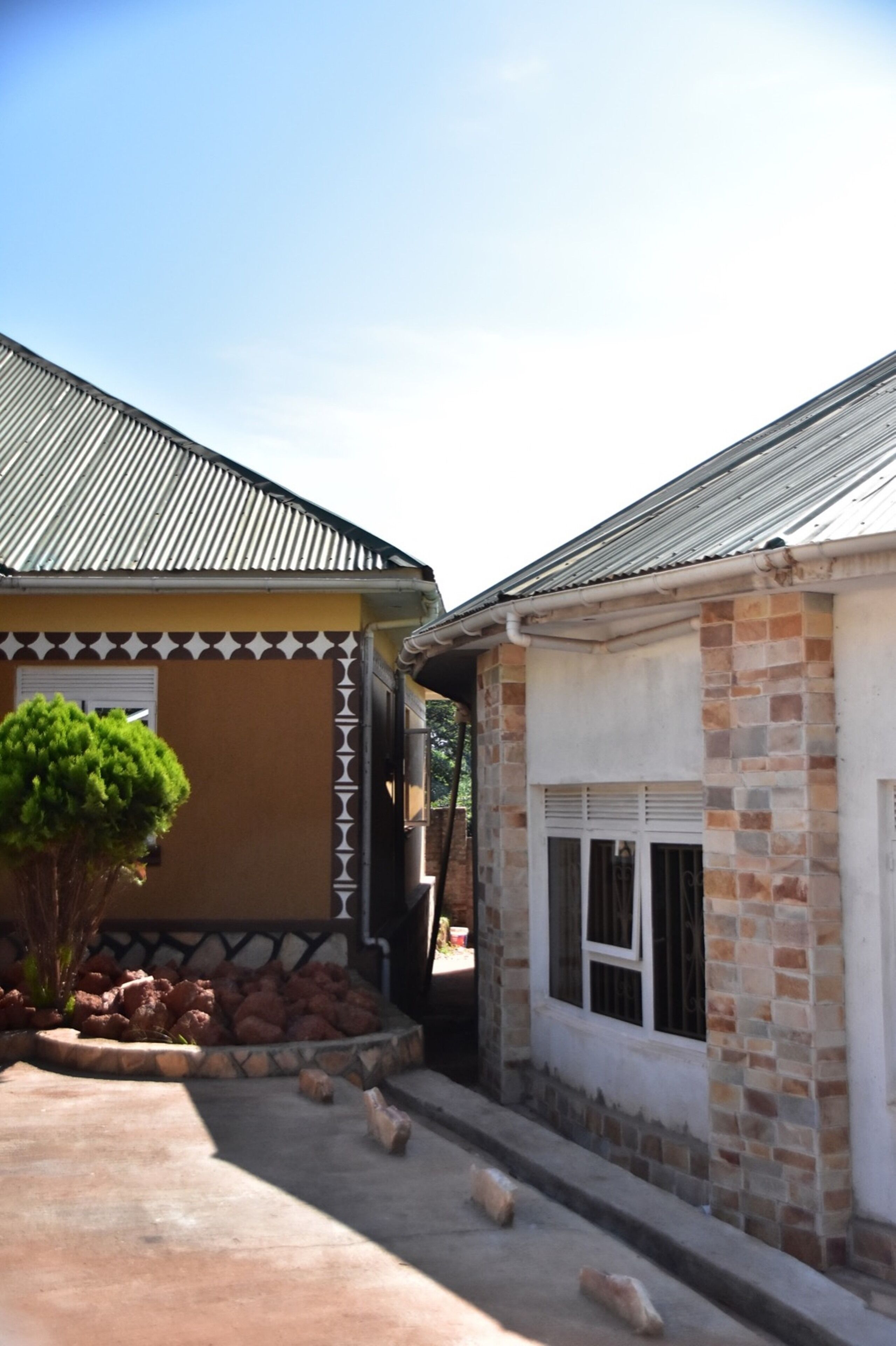A building with a tiled roof, a small garden with a tree, and a paved entrance.