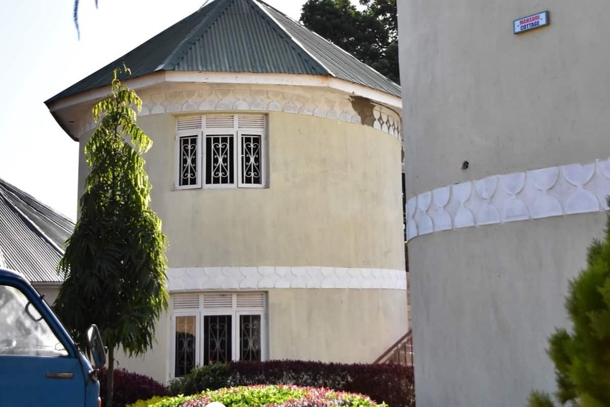 A building with a curved roof, a sign indicating it is a guest house, and a well-maintained garden with a lamp post.