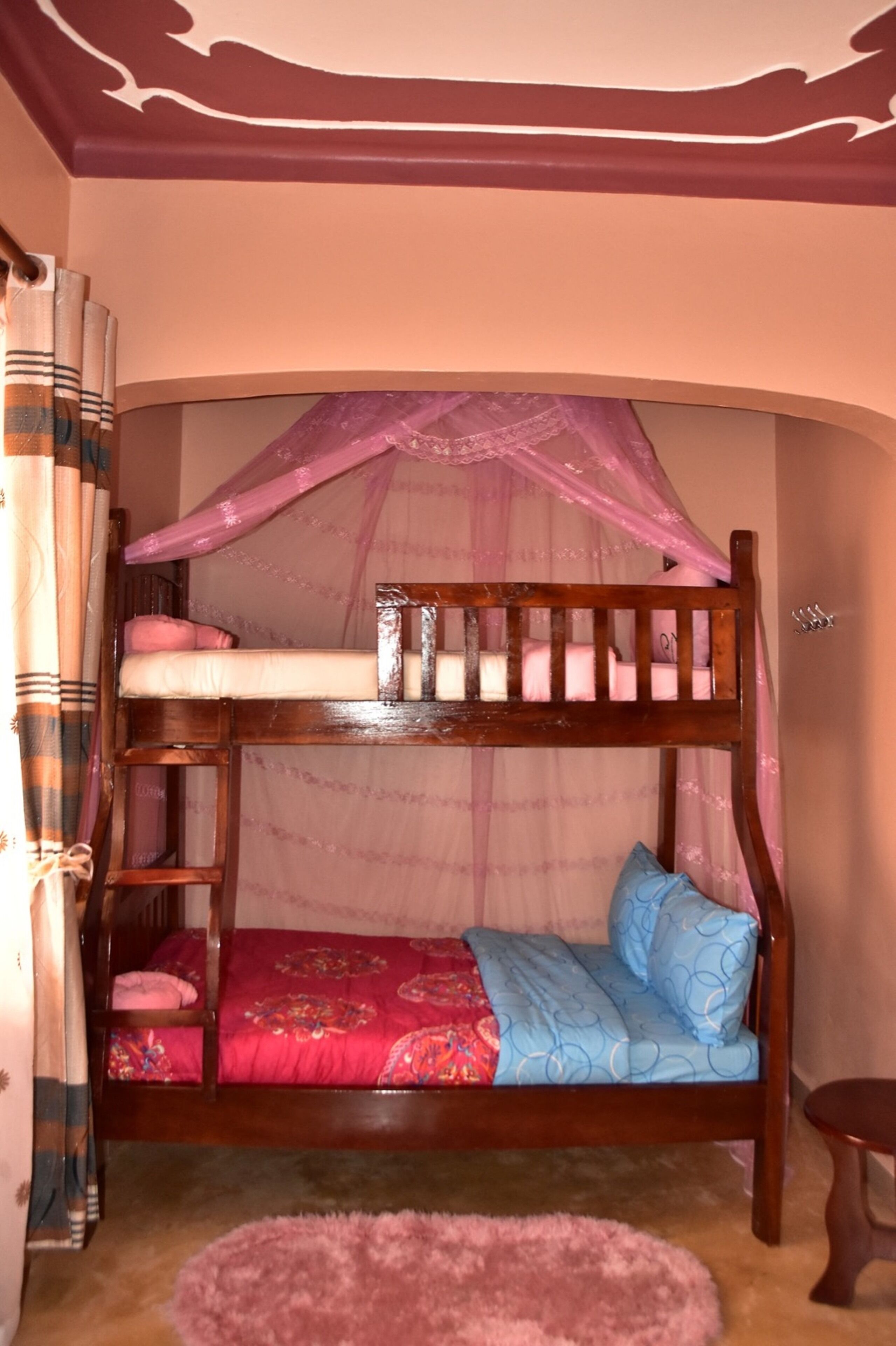 Una cama individual con dosel, una mesita pequeña y una alfombra rosa.