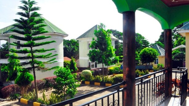 A courtyard with a variety of trees and shrubs, a white building with a green roof, and a black metal railing.