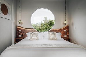Ein Schlafzimmer mit einem großen Rundfenster, einem hölzernen Kopfteil, weißer Bettwäsche und zwei Nachttischen mit Lampen.