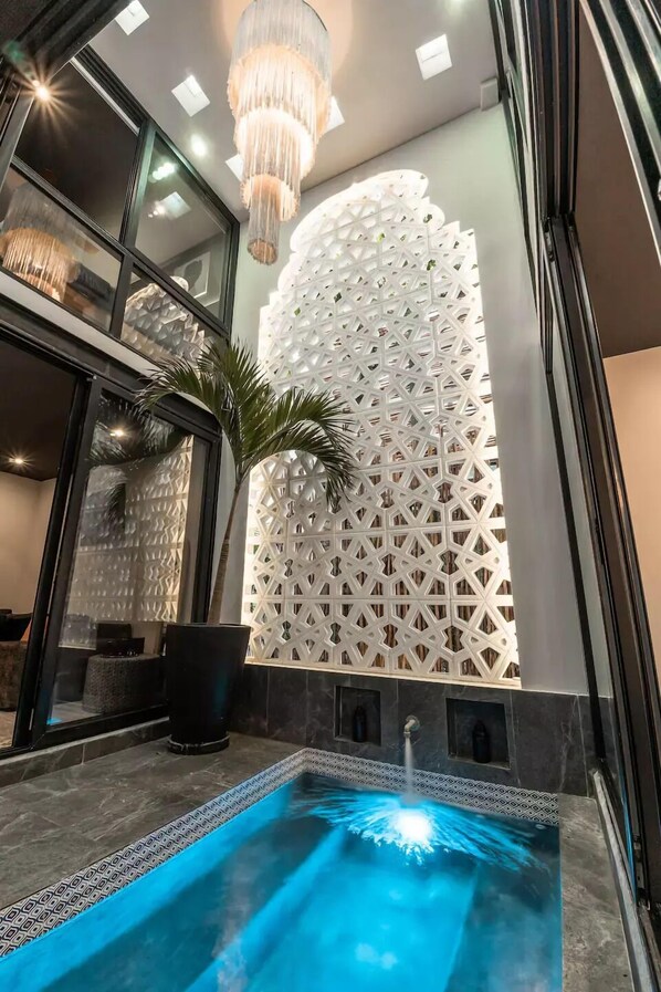 Ein moderner Innenpoolbereich mit geometrischem Wanddesign, einer hängenden Leuchte und einem Pool in leuchtendem Blau.