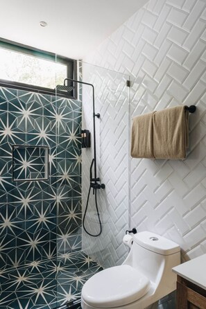 Ein Badezimmer mit Duschkabine mit geometrischen Fliesen, Toilette und Handtuchhalter.