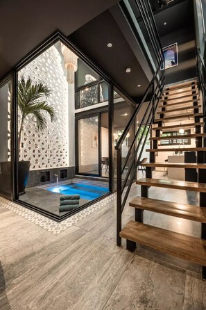 A modern interior with a glass-enclosed pool, a wooden staircase, and a geometric wall design.