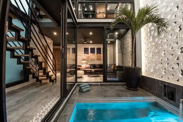 Um interior moderno com piscina, escada e área de estar com sofá e luminárias.