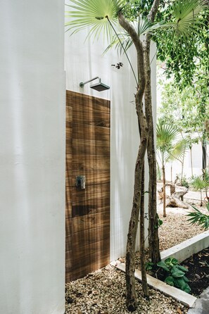 Casa de banho moderna com porta de madeira, chuveiro com chuveiro manual verde e uma pequena área com plantas, incluindo uma árvore e uma palmeira.