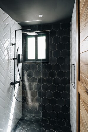 En dusch med ett svart, hexagonformat kakelmönster, ett fönster och en vägg av trä.