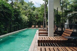 Ein Poolbereich mit Holzliegen und einem klaren Pool, umgeben von üppiger Vegetation.