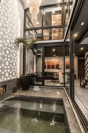 Ein modernes Interieur mit einem gläsernen Wohnbereich, einem poolförmig gefliesten Pool und einer Treppe, die zu einer oberen Ebene führt.
