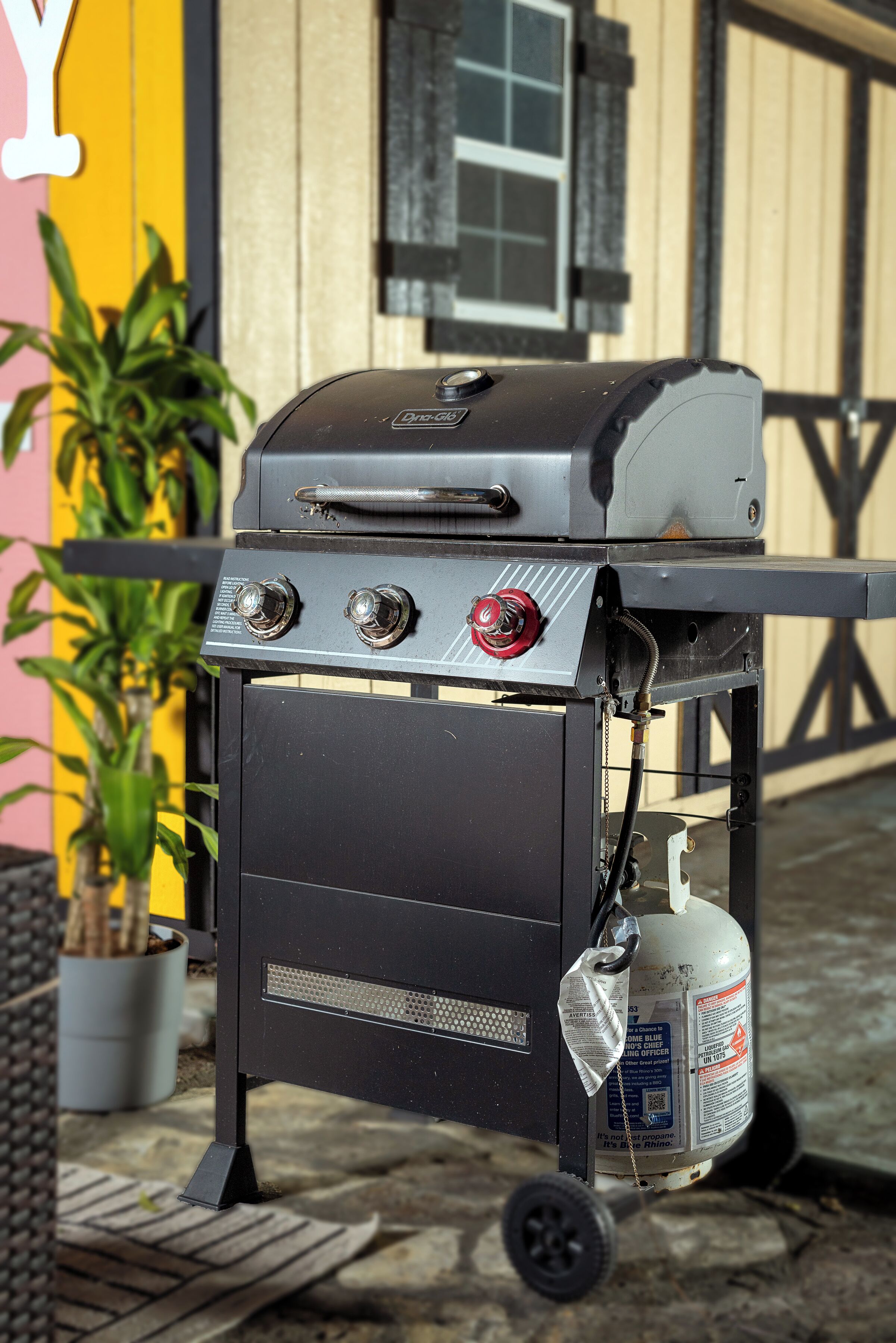 Een draagbare grill met een gasfles, geplaatst op een wielen voorzien karretje.