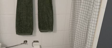 Une salle de bain équipée de toilettes, de deux serviettes, d’un rideau de douche et d’un sol carrelé.