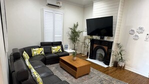 Een woonkamer met een zwarte leren bank, een houten salontafel, een flatscreen televisie, een open haard en decoratieve wandkunst.