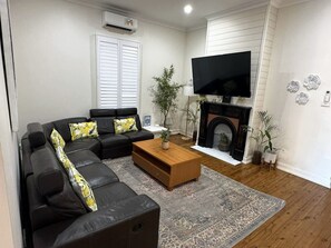 A living room with a black leather sofa, a wooden coffee table, a flat-screen TV, a fireplace, and decorative wall art.