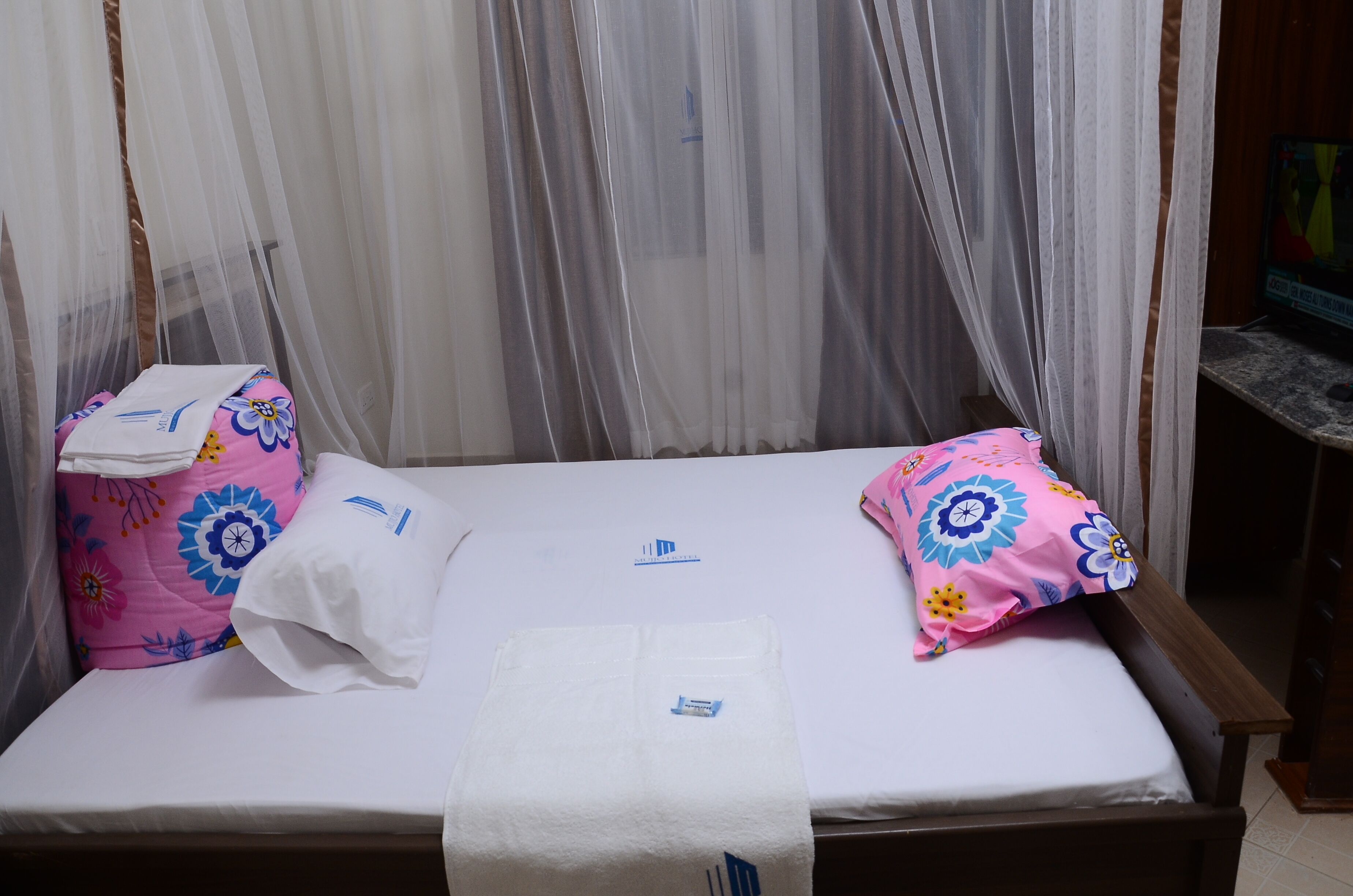 Un lit avec un drap blanc, deux coussins à motifs floraux roses et une serviette blanche.