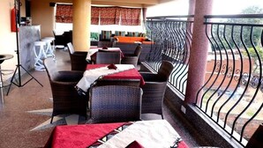 Un espacio de estar al aire libre cubierto, con muebles de mimbre y un balcón con barandilla de hierro forjado.