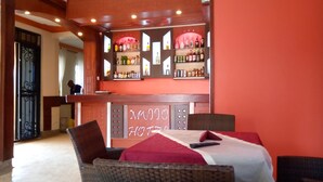 Zona de bar con pared roja, estantes llenos de botellas de licores y sillas de mimbre con cojines rojos.