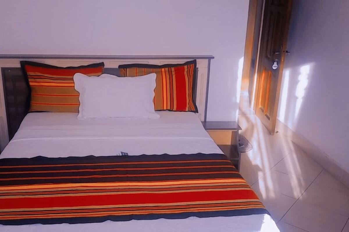 Ein Bett mit gestreifter Bettwäsche, einem Kopfteil und einem Fenster mit Vorhängen.