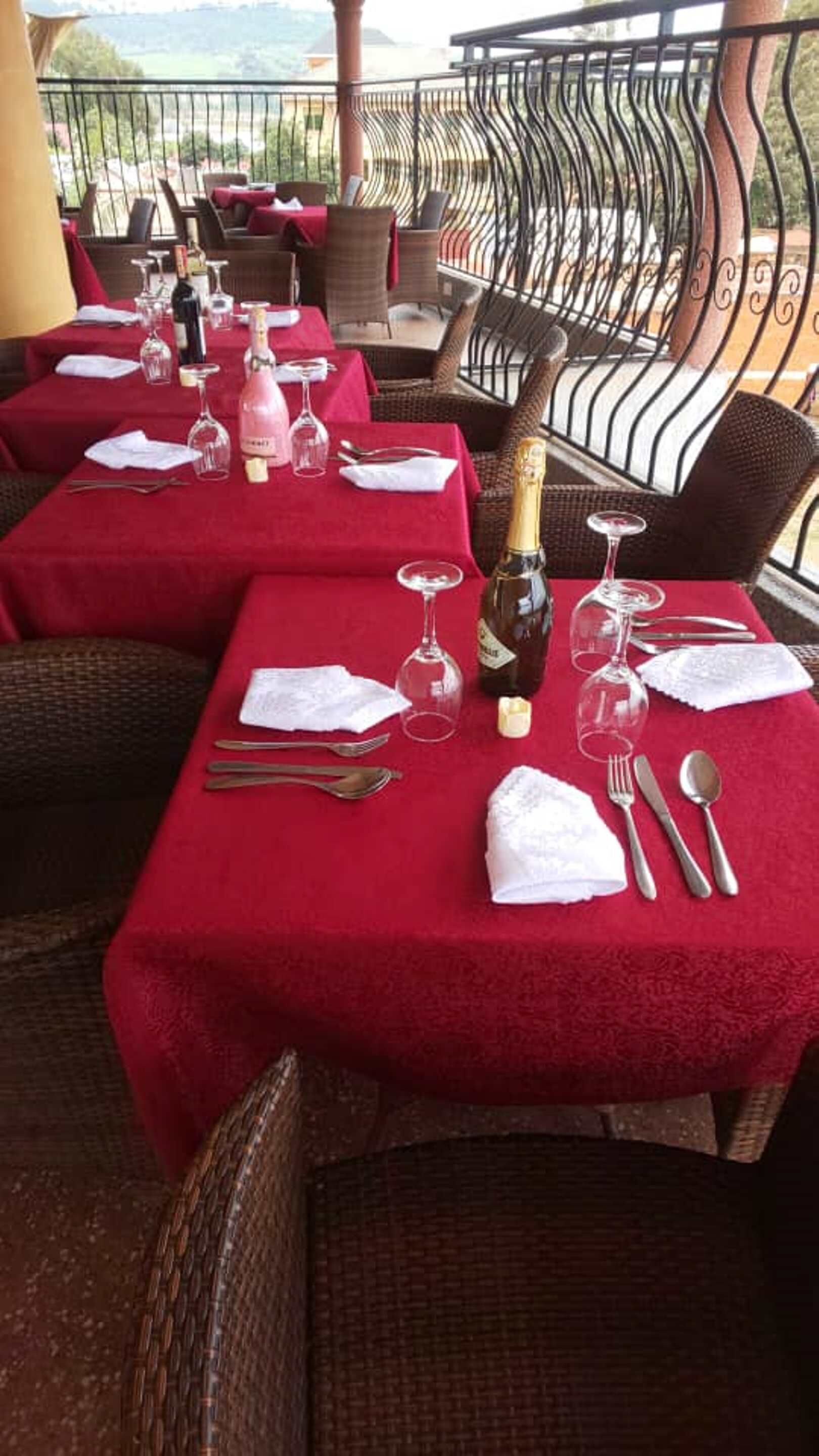A restaurant terrace with red tablecloths, wicker chairs, and a view of the countryside.