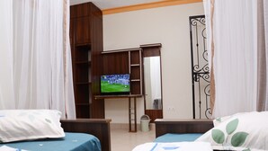 Habitación de hotel con dos camas, un televisor sobre un soporte, un armario y un baño con cortina de ducha.