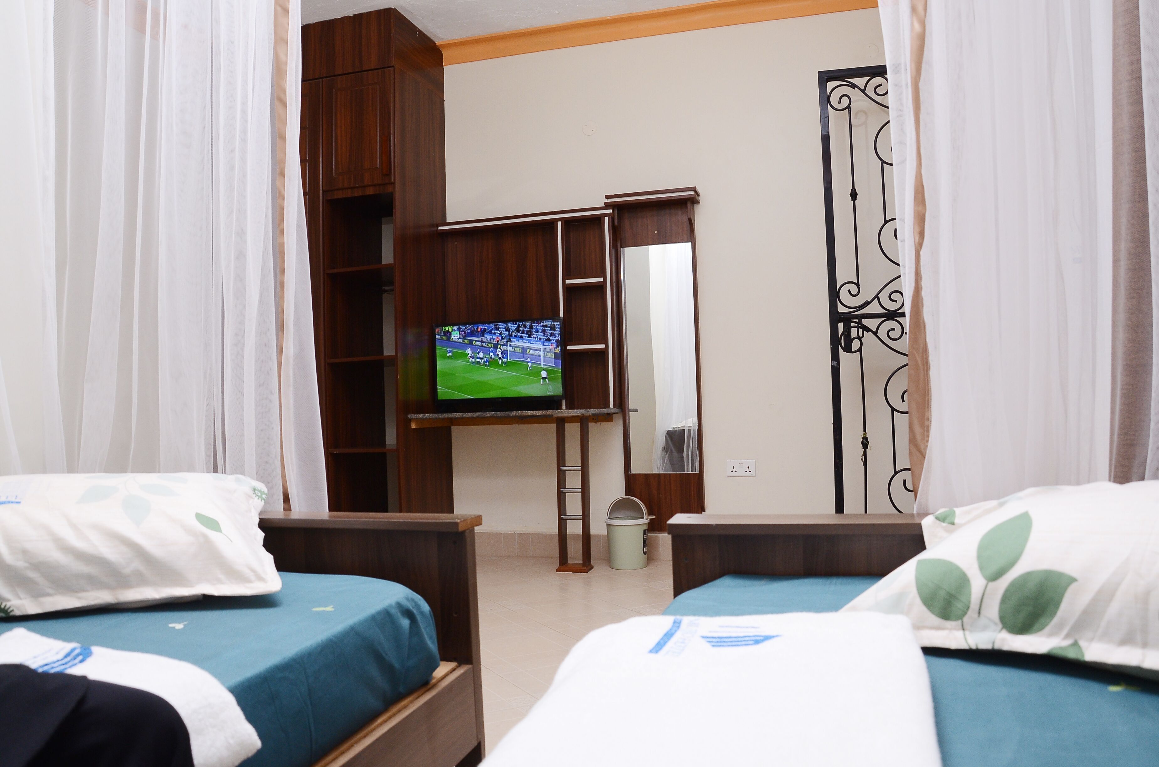 A hotel room with two beds, a TV on a stand, a wardrobe, and a mirror.