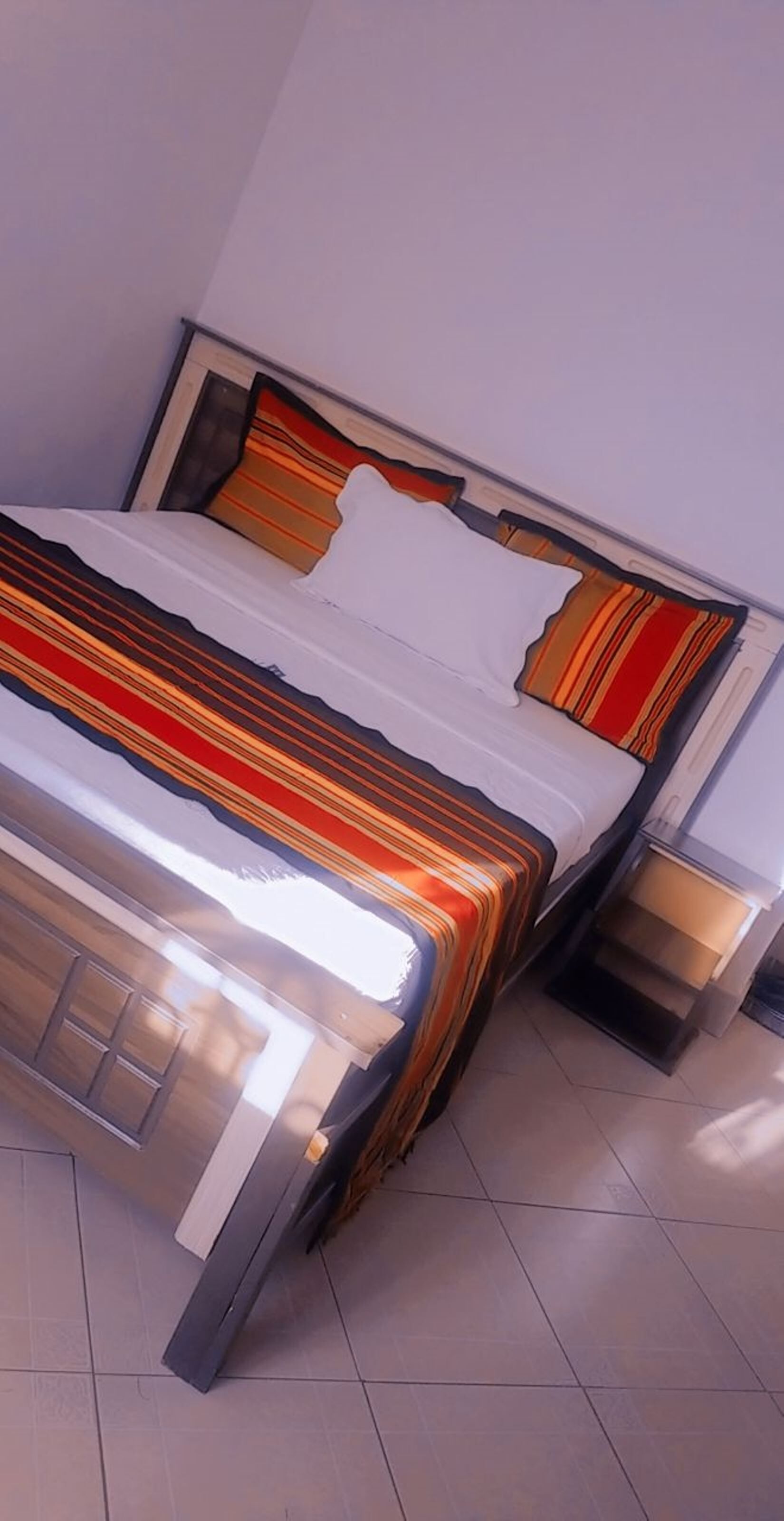 A bed with a striped bedspread, a white pillow, and a headboard with a striped pattern. There is a nightstand with a lamp beside the bed.