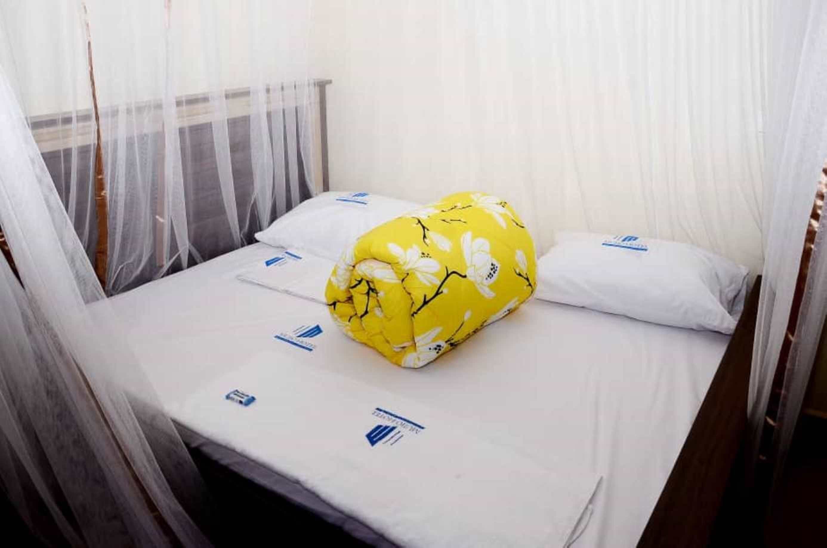 Een bed met klamboe, witte beddengoed en een geel bloemenkussen.