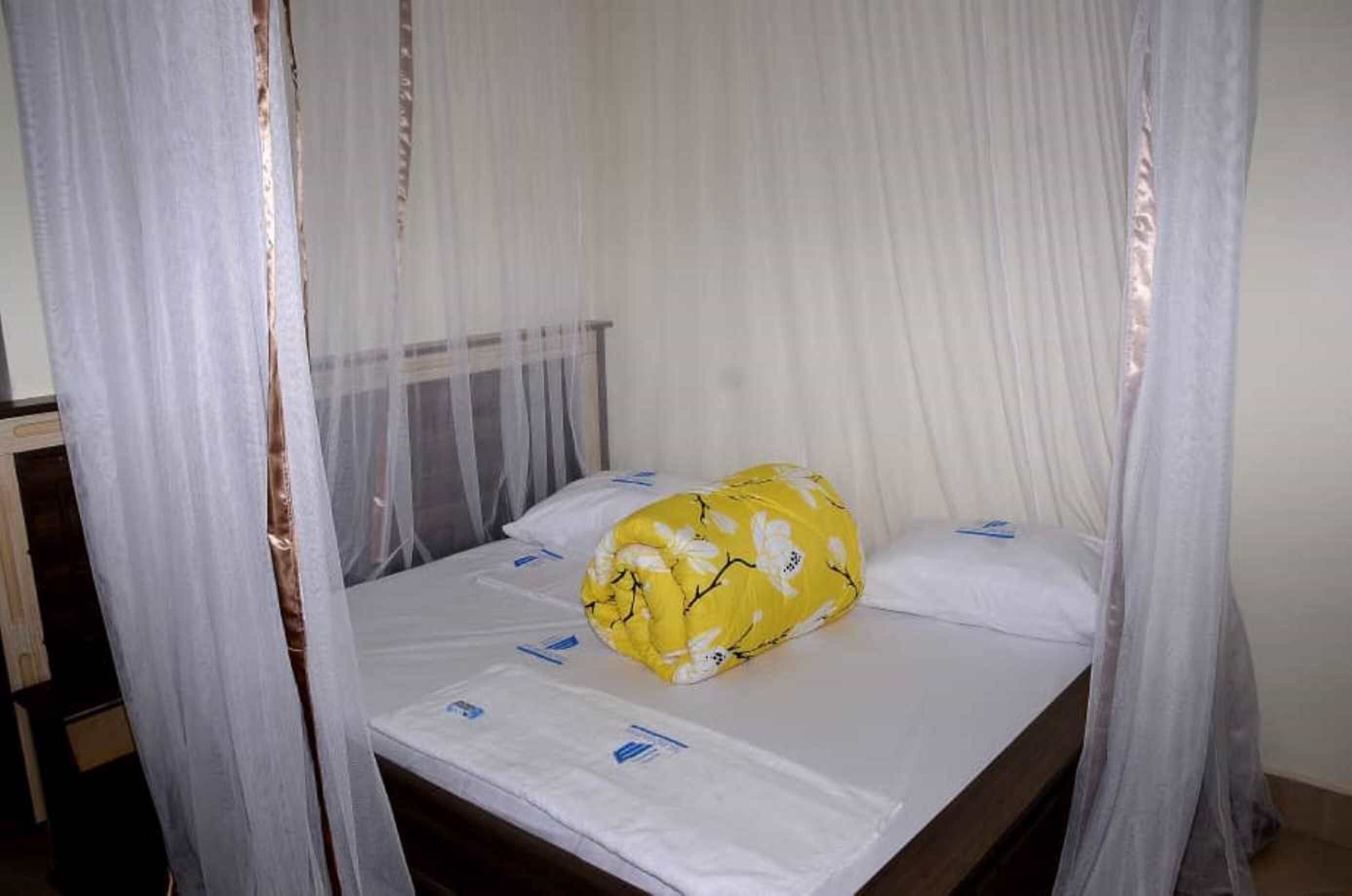 A single bed with a mosquito net, a yellow floral pillow, and a white sheet.